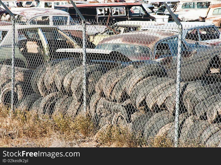 Old vehicles being recycled for parts and scrap metal in an auto salvage yard. used tires in the foreground