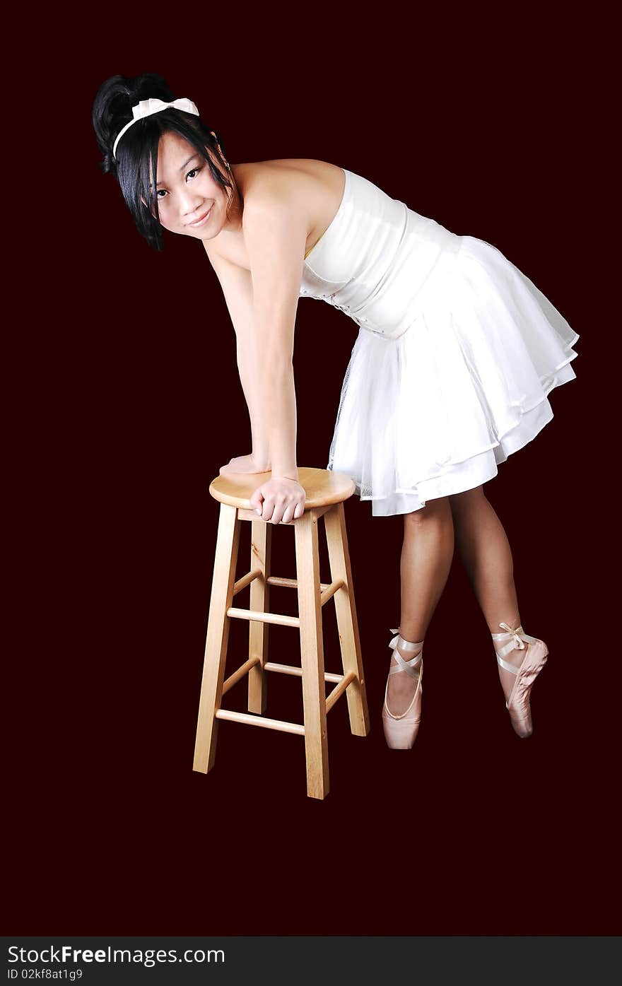 A Chinese ballet dancer in a white dress standing on a chair and on her toes in ballet slippers, for dark burgundy background. A Chinese ballet dancer in a white dress standing on a chair and on her toes in ballet slippers, for dark burgundy background.