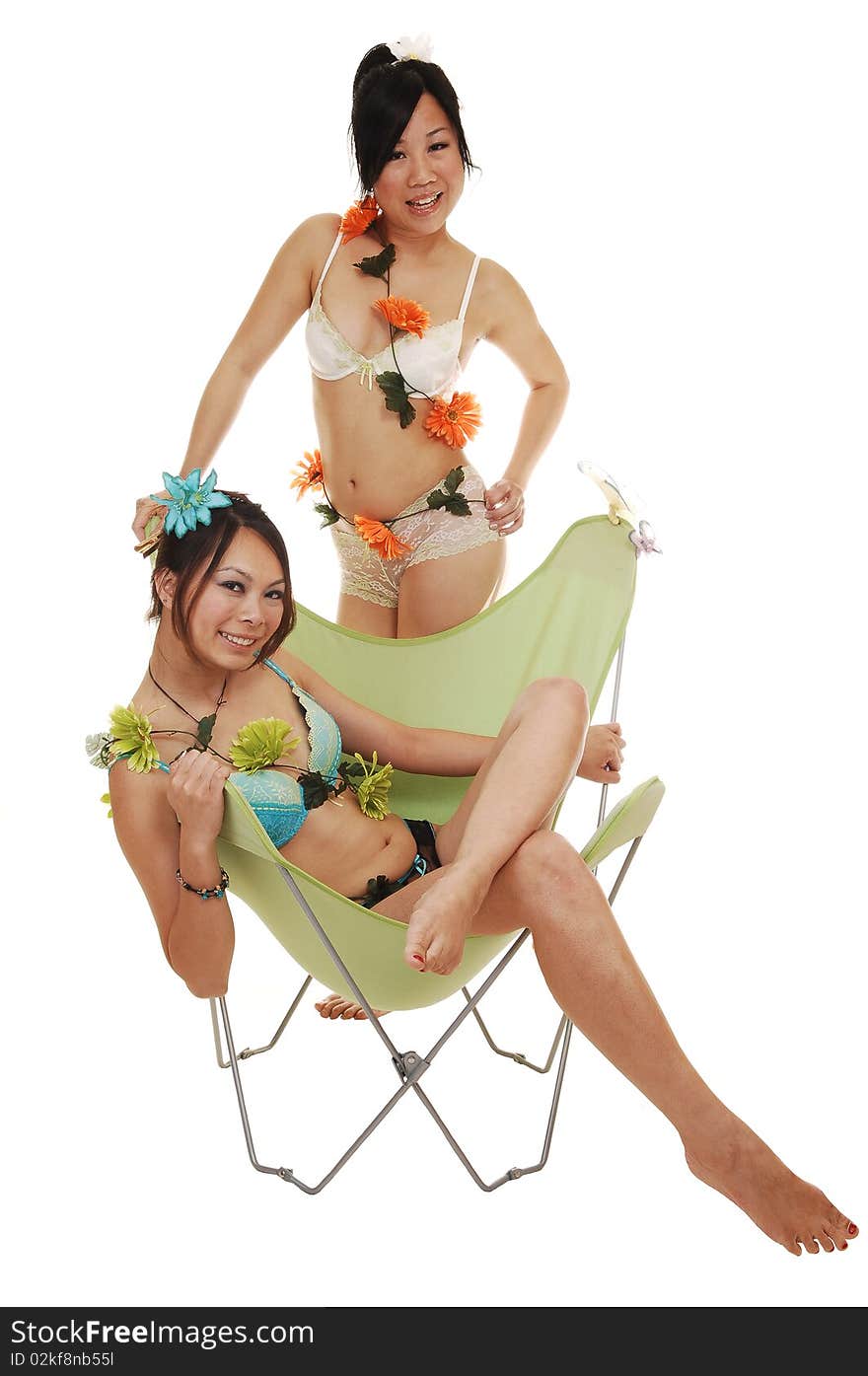 Two pretty Asian girls in lingerie, one sitting in a chair, the other one standing behind, with flowers around there bodies for white background. Two pretty Asian girls in lingerie, one sitting in a chair, the other one standing behind, with flowers around there bodies for white background.