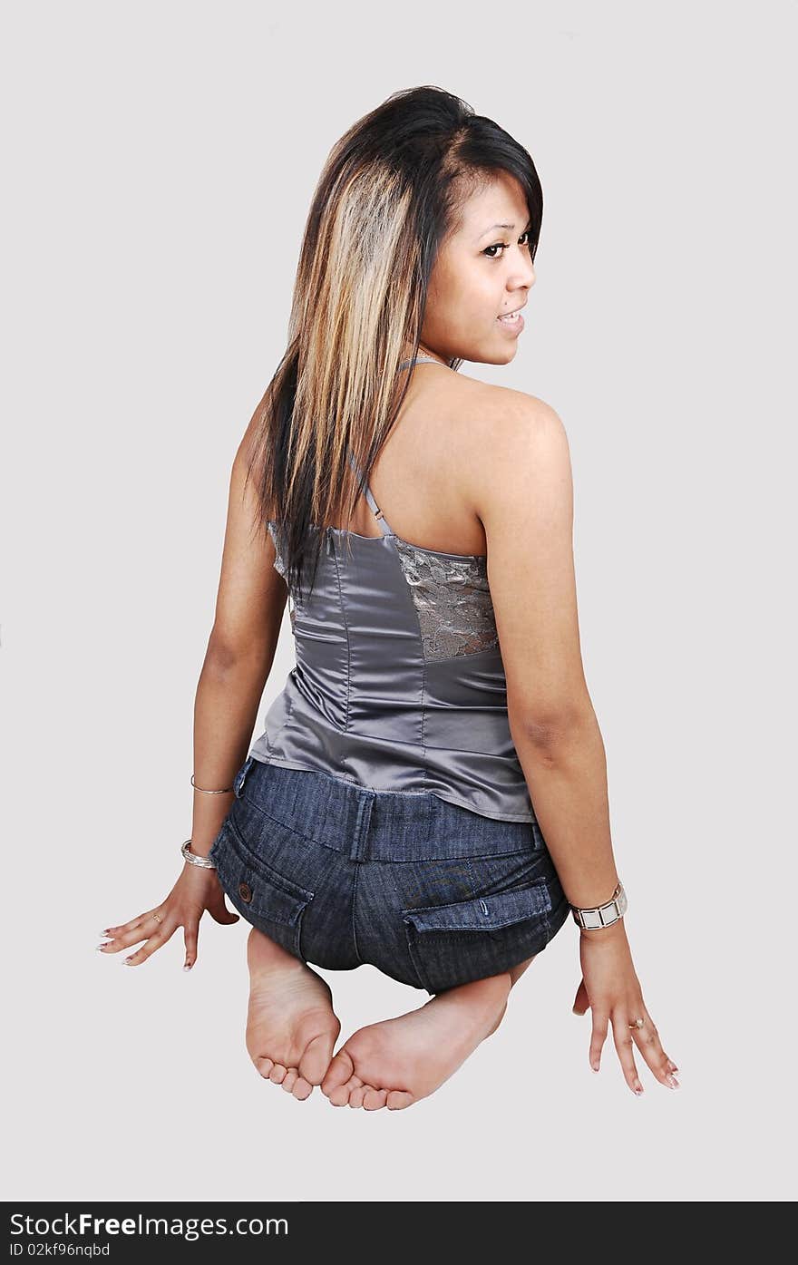 A young pretty Asian woman, in shorts and silver gray top, kneeling on the floor in the studio and looking over her shoulder, on white background. A young pretty Asian woman, in shorts and silver gray top, kneeling on the floor in the studio and looking over her shoulder, on white background.