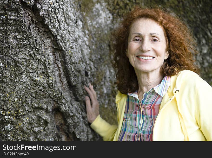 Portrait of a Pretty Senior Woman With Red Hair Touching a Treetrunk. Portrait of a Pretty Senior Woman With Red Hair Touching a Treetrunk