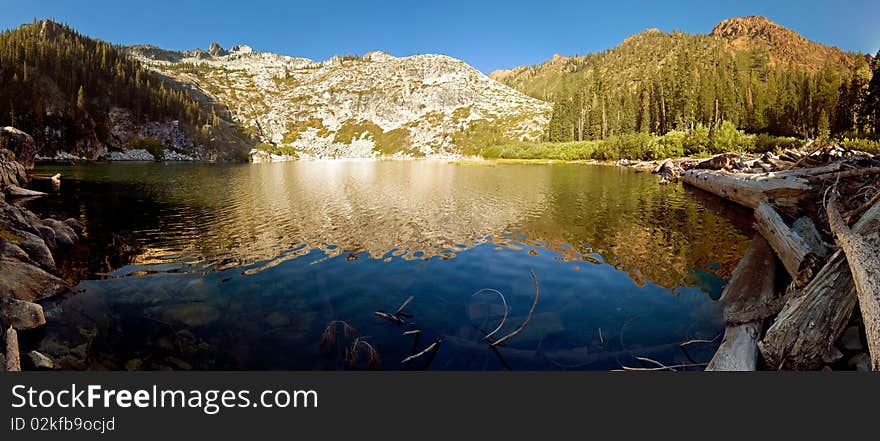 Clear pristine alpine lake flanked by granite peaks and logs. Clear pristine alpine lake flanked by granite peaks and logs.