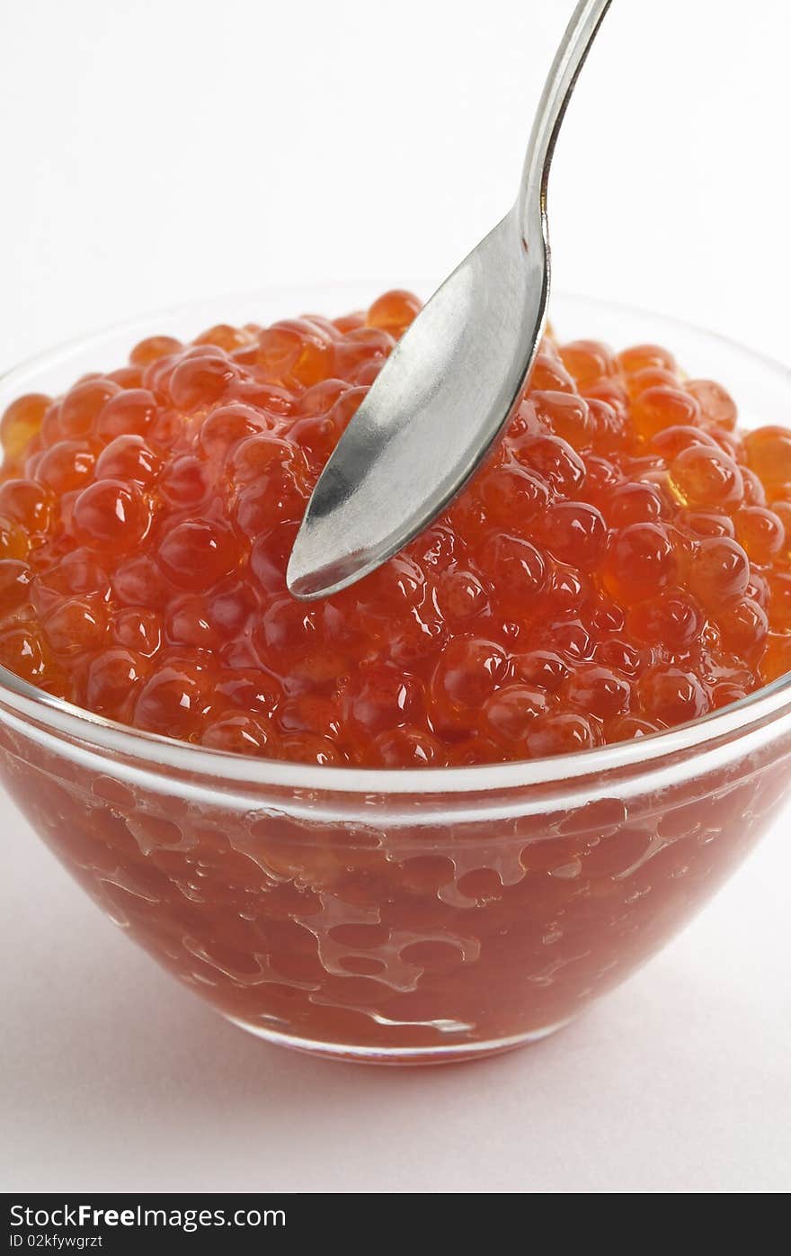 Red caviar in the little glass bow and spoon fragment isolated over white background