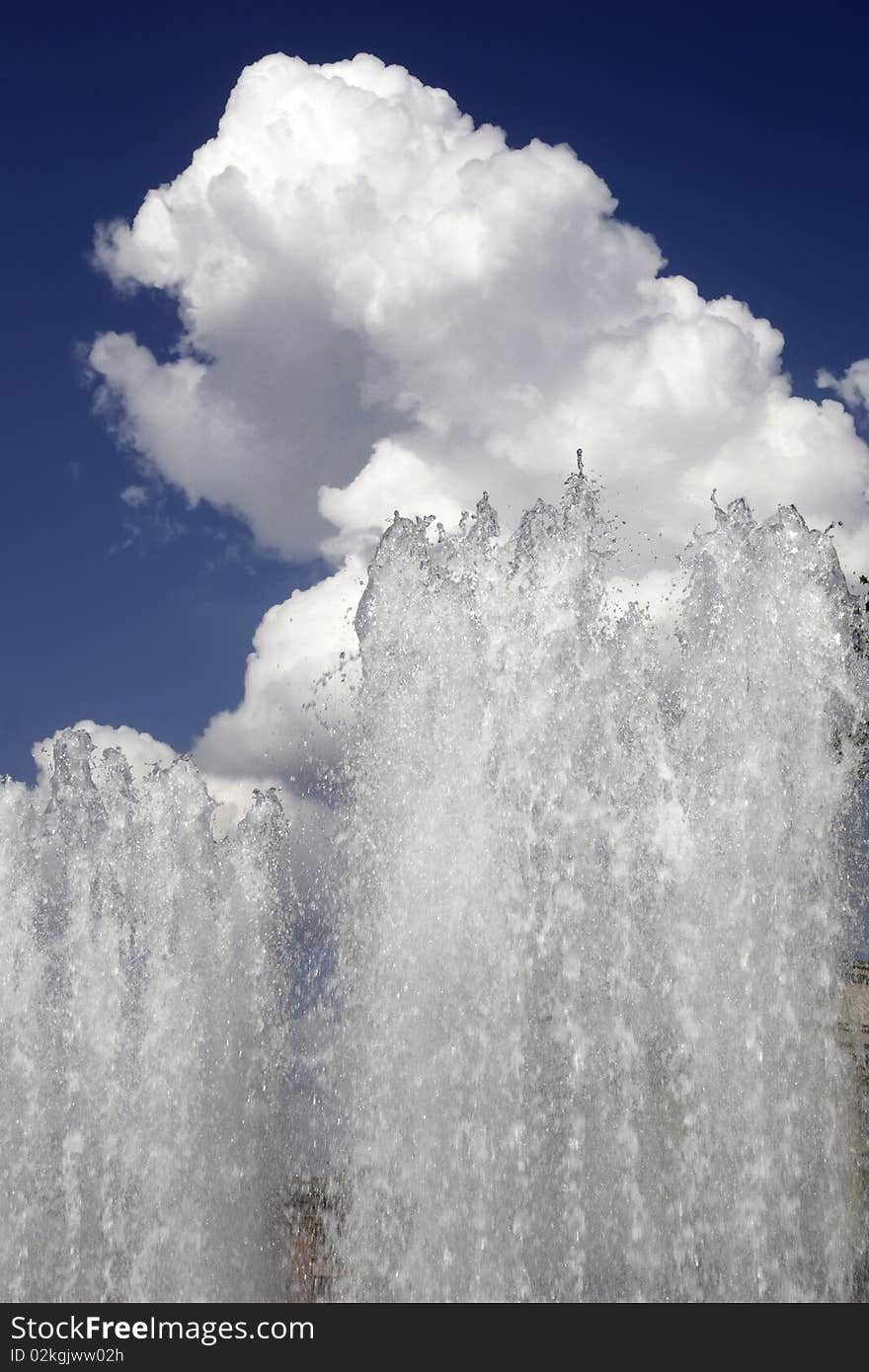 Streams of a fountain against the sky and a cloud