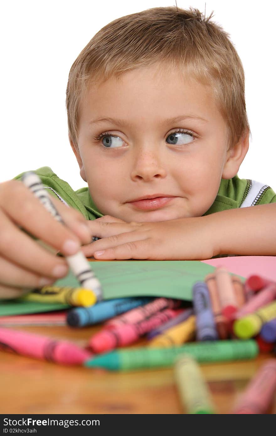 Young blond boy resting his head on his hand, crayons and colorful paper in front of him. Young blond boy resting his head on his hand, crayons and colorful paper in front of him