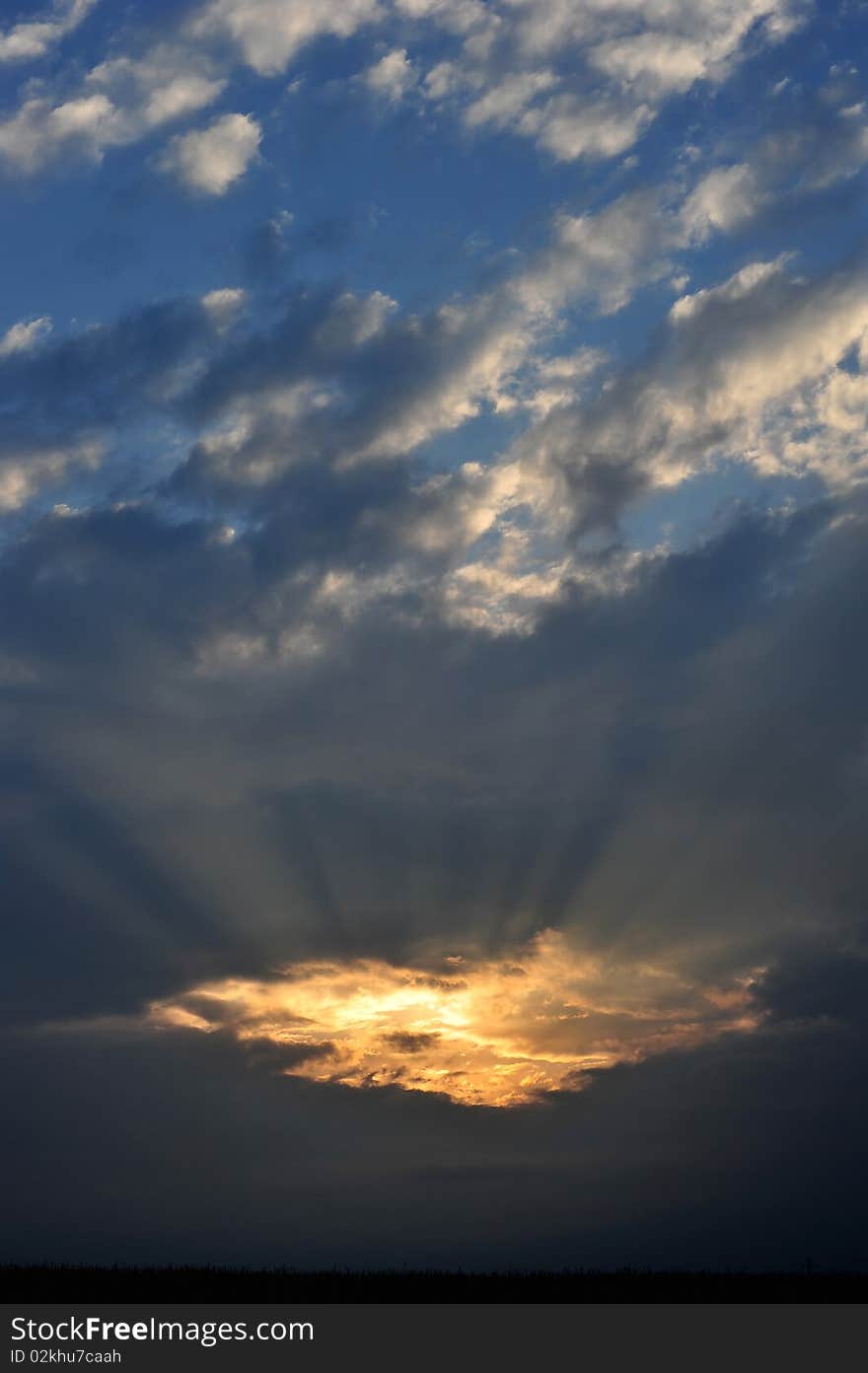 Spectacular sunset behind clouds with orange and blue sky