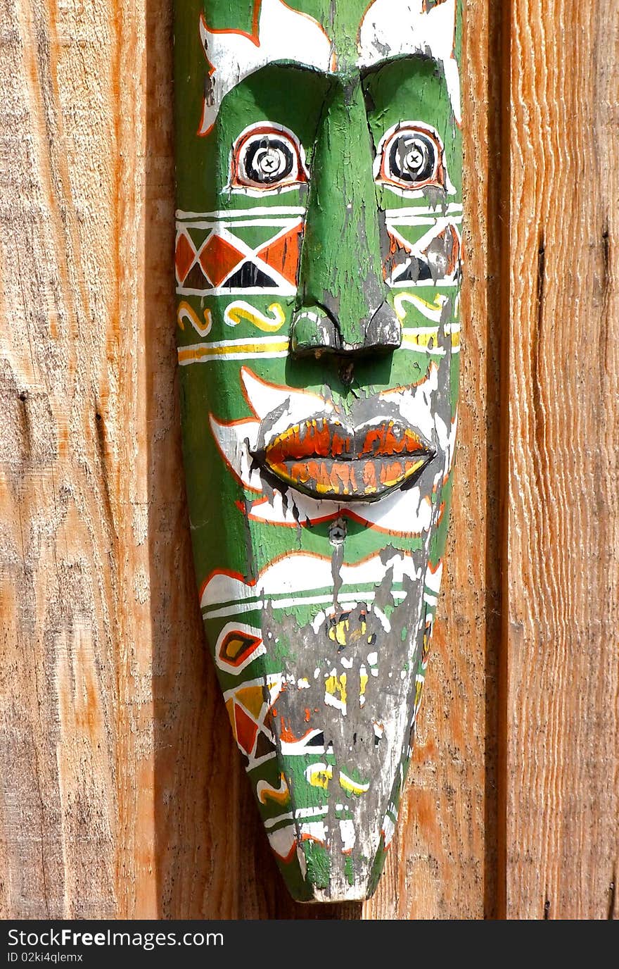 A detailed painted wooden mask hung against wooden paneling. A detailed painted wooden mask hung against wooden paneling.