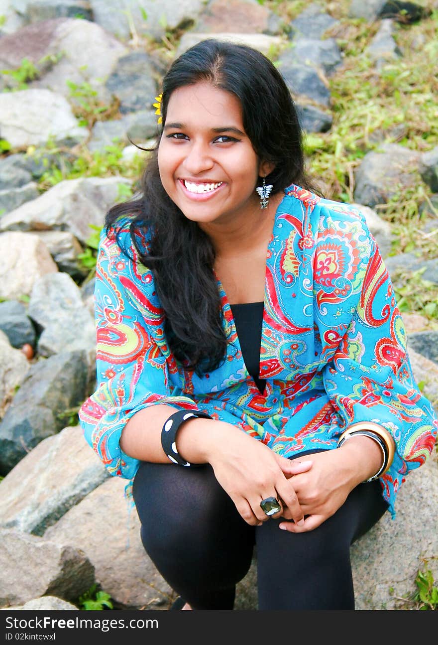 A young and beautiful pakistani model sitting on rocky ground having a bright smile on her face