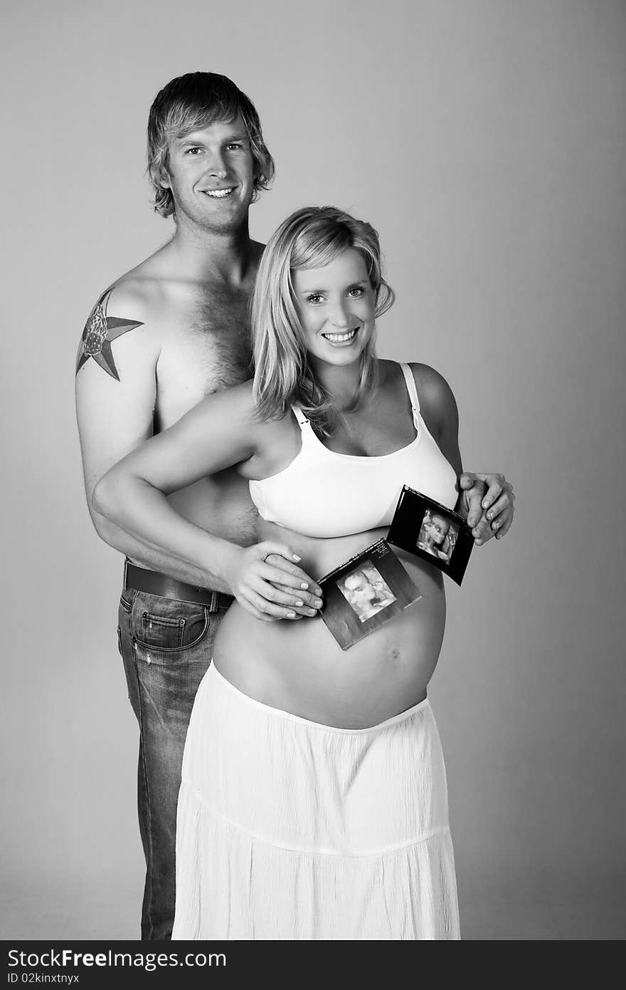 A young, pregnant woman is smiling as she stands in front of a man holding photographs of her ultrasound. Vertical shot. A young, pregnant woman is smiling as she stands in front of a man holding photographs of her ultrasound. Vertical shot.