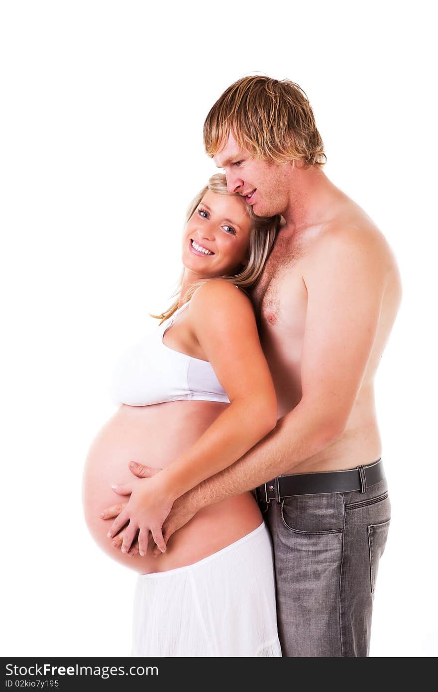 Shirtless young couple stand affectionately with the husband holding his pregnant wife in his arms. Isolated on white. Shirtless young couple stand affectionately with the husband holding his pregnant wife in his arms. Isolated on white.