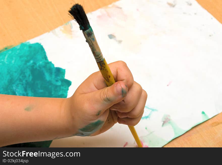 Child hand holding a brush on a watercolor paint. Child hand holding a brush on a watercolor paint