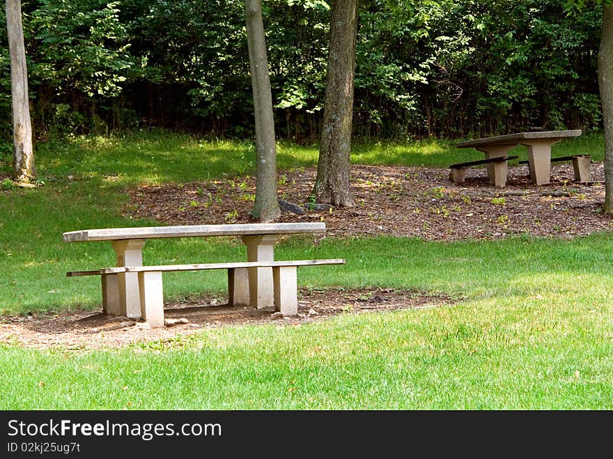 A pair of picnic tables in a wooded area of a public park.