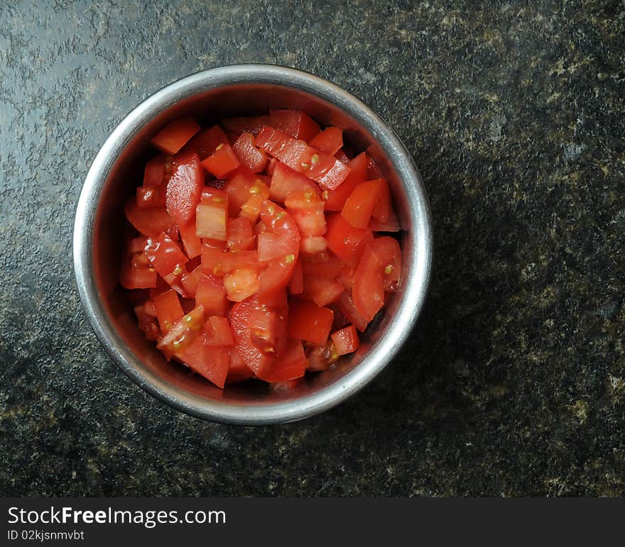 A bunch of sliced, diced, and cut red tomatoes inside of a round metal bowl resting on a kitchen counter top. A bunch of sliced, diced, and cut red tomatoes inside of a round metal bowl resting on a kitchen counter top
