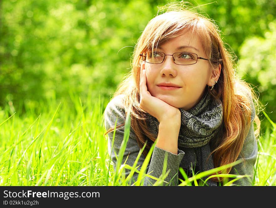 The young girl, in glasses, lays on a green grass, in park. The young girl, in glasses, lays on a green grass, in park