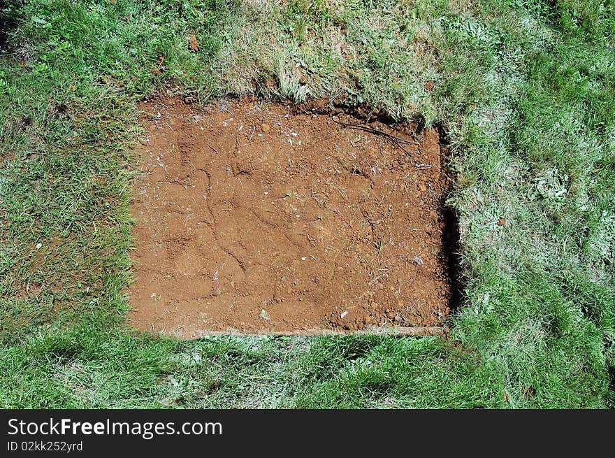 A flat dirt patch is surrounded by green grass. This is really a filled hole with dirt. A flat dirt patch is surrounded by green grass. This is really a filled hole with dirt.