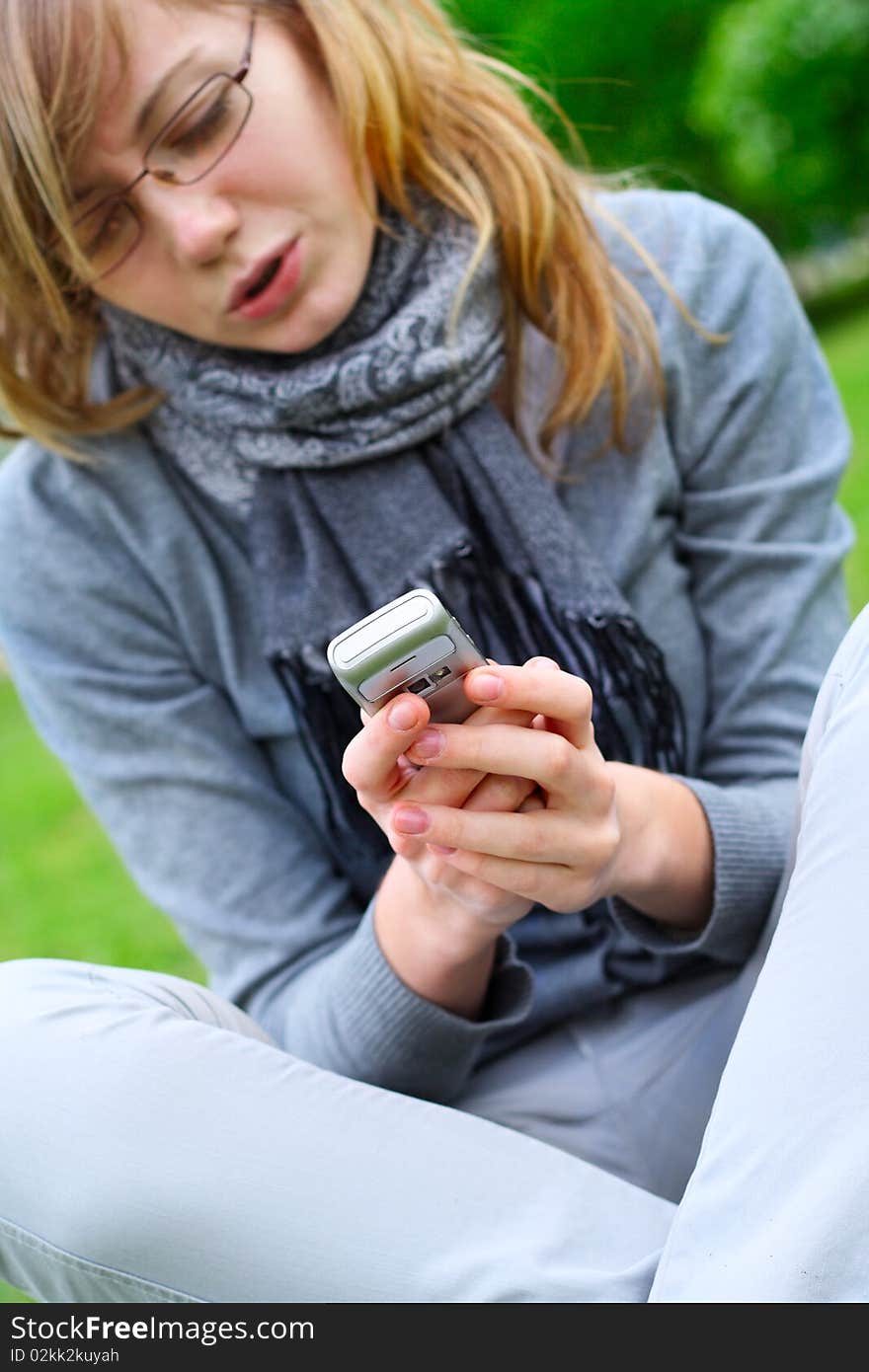 The girl sits, and holds a mobile phone in hands. The girl sits, and holds a mobile phone in hands