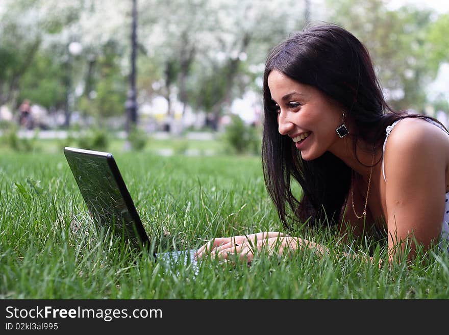 Young woman with laptop lying jn the green grass