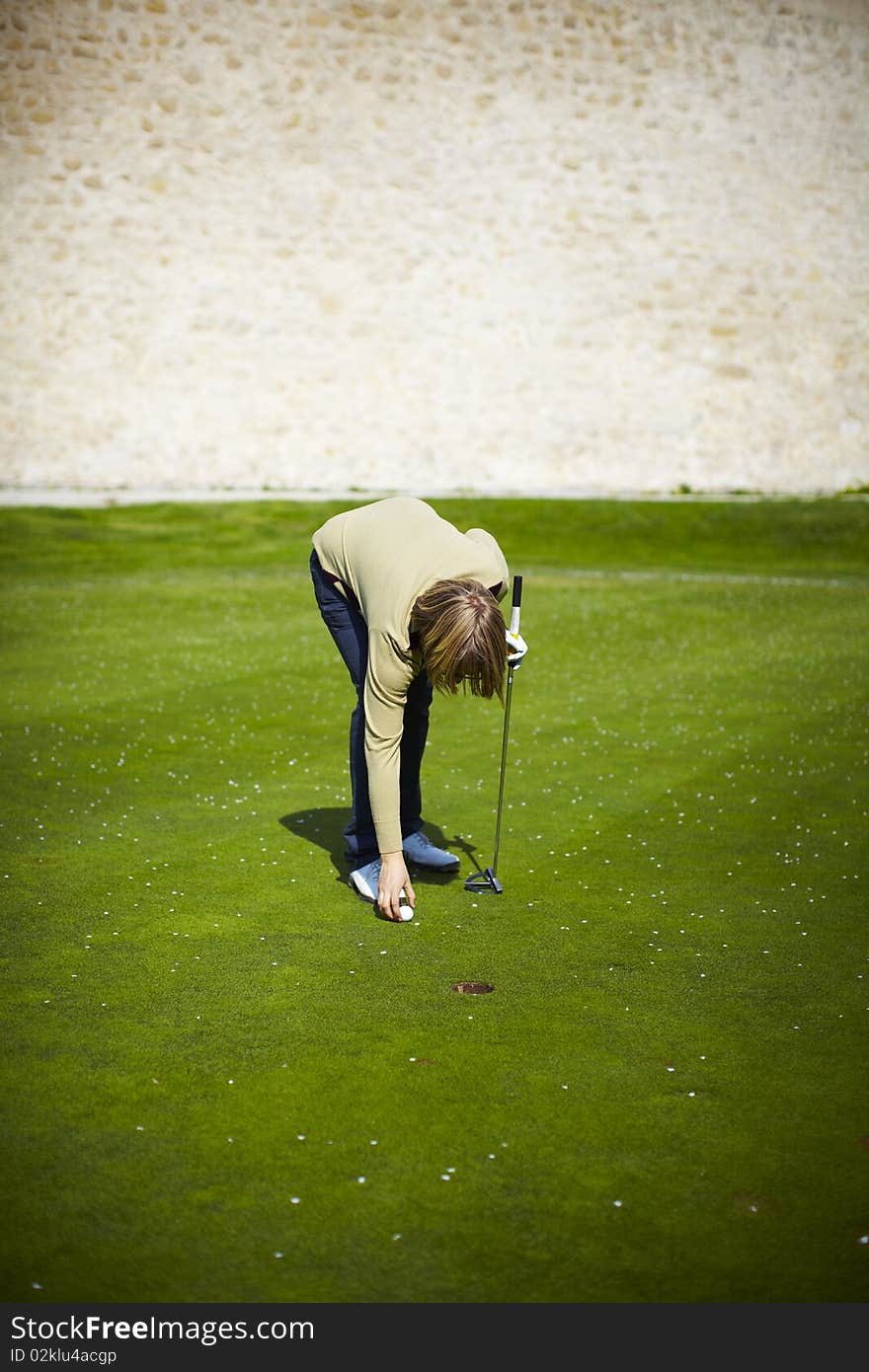 Woman at the golf range preparing golf ball and stone wall on a background.