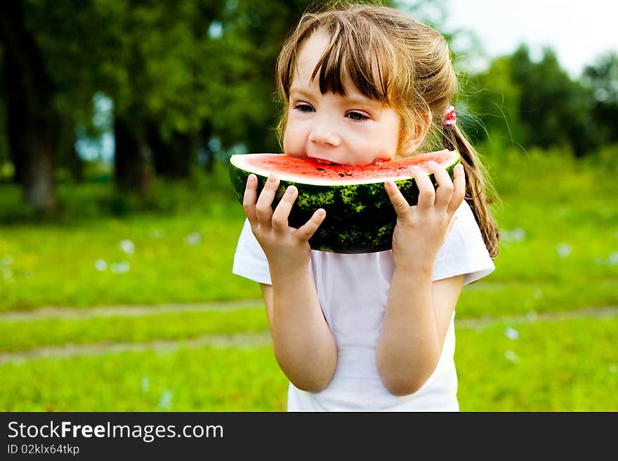 Cute little girl eating watermelon on the grass in summertime