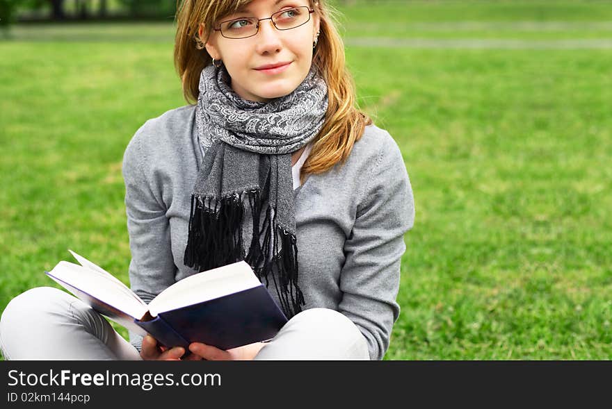 The girl sits on a grass, reads the book