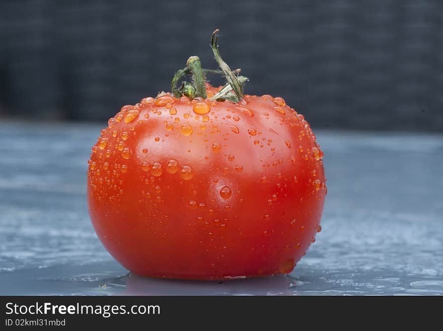 One wet tomato on a blue table in the rain