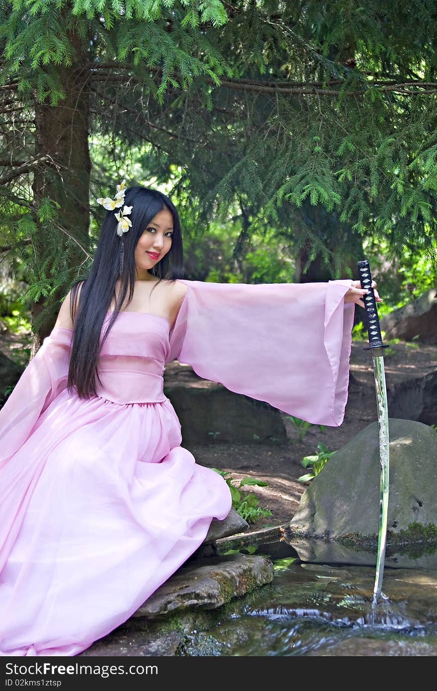 Beutiful japanese woman in pink dress sitting on the stone wields a katana