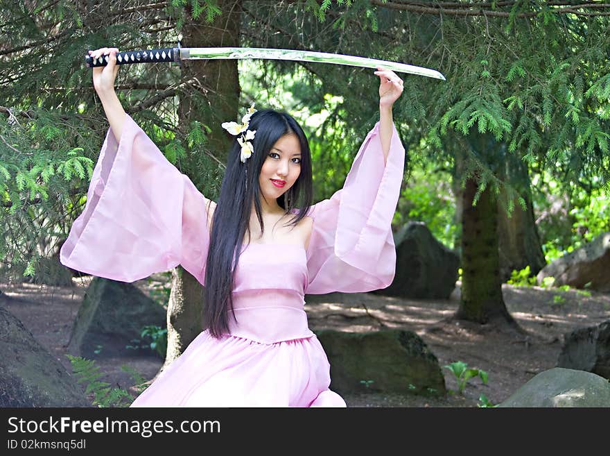 Beutiful japanese woman in pink dress sitting on the stone wields a katana