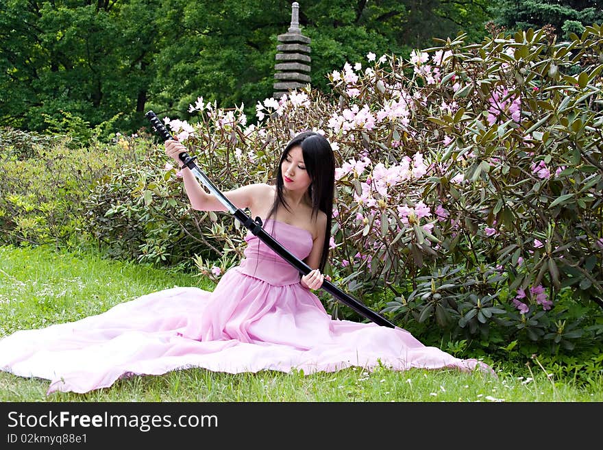 Beautiful asian woman in a pink dress sitting on the ground with a sword in the hands. Beautiful asian woman in a pink dress sitting on the ground with a sword in the hands