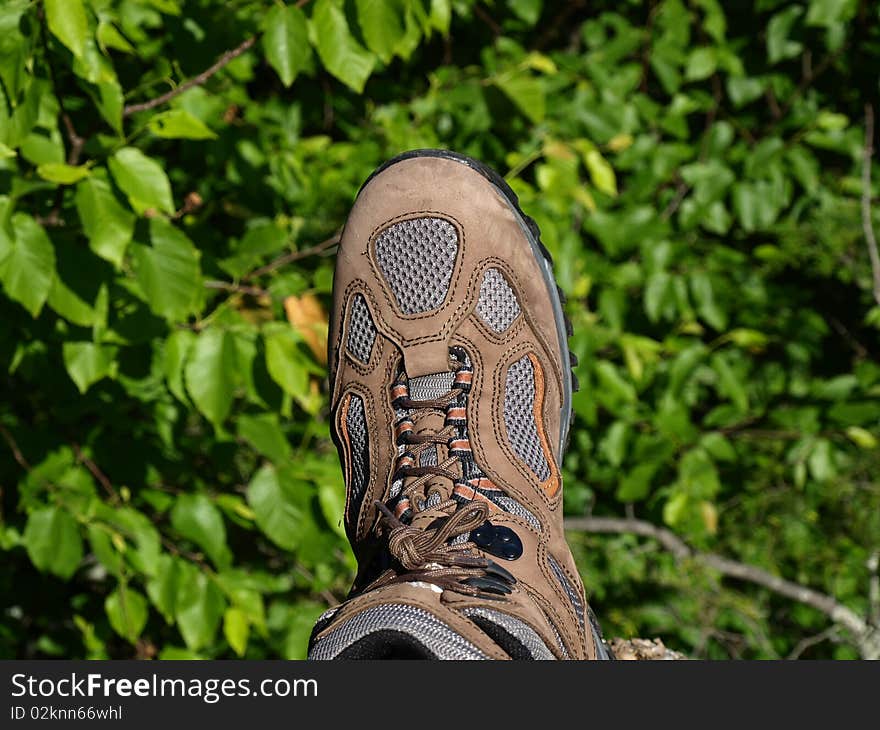 One foot hanging on the edge of mountain side.  A brown hiking boot. One foot hanging on the edge of mountain side.  A brown hiking boot.