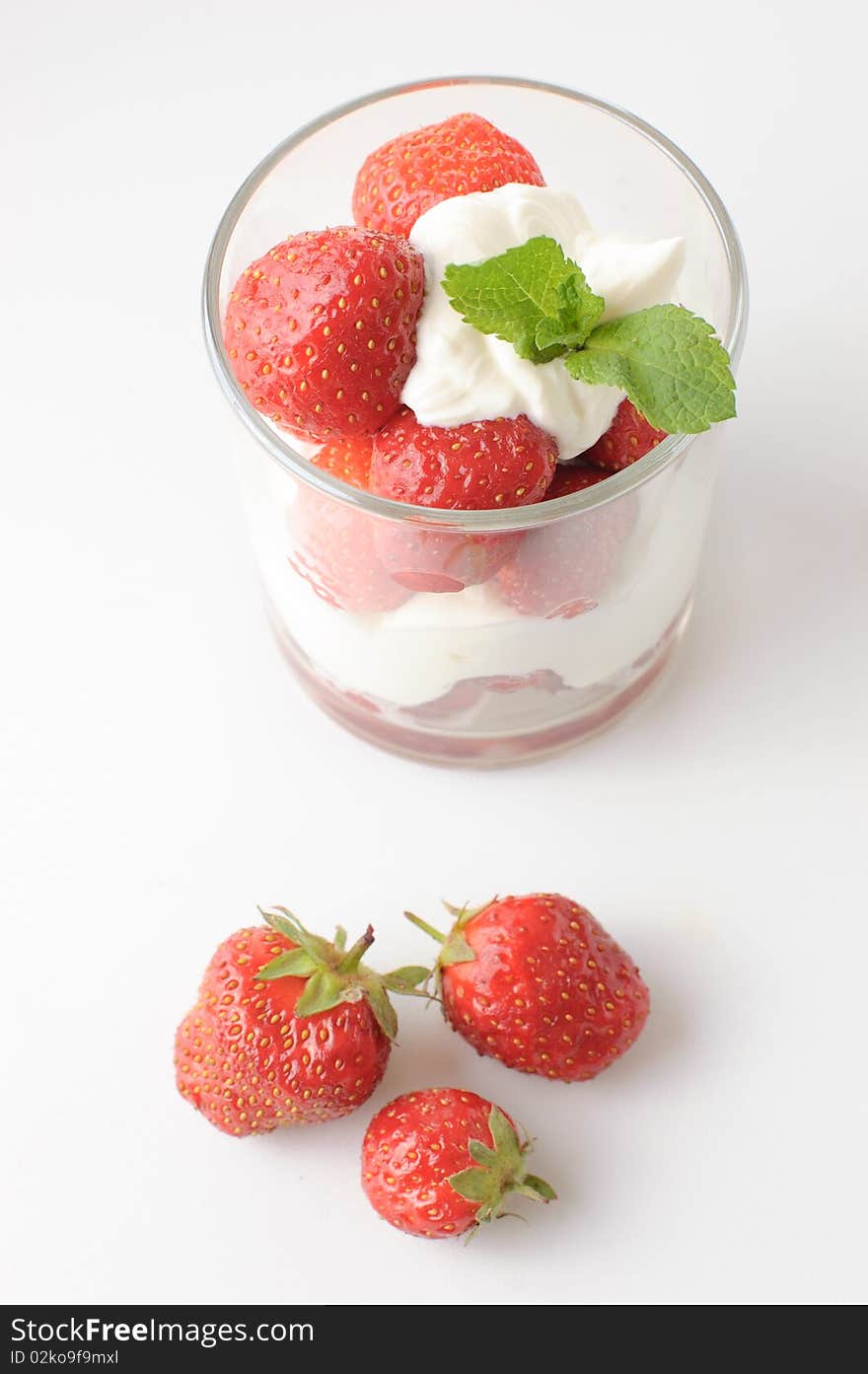 Strawberries with whipped cream and mint leaf in a glass on a white background