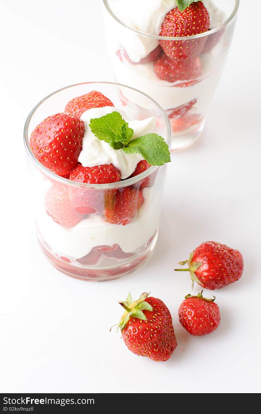 Two cups with strawberry dessert with a mint leaf on a white background