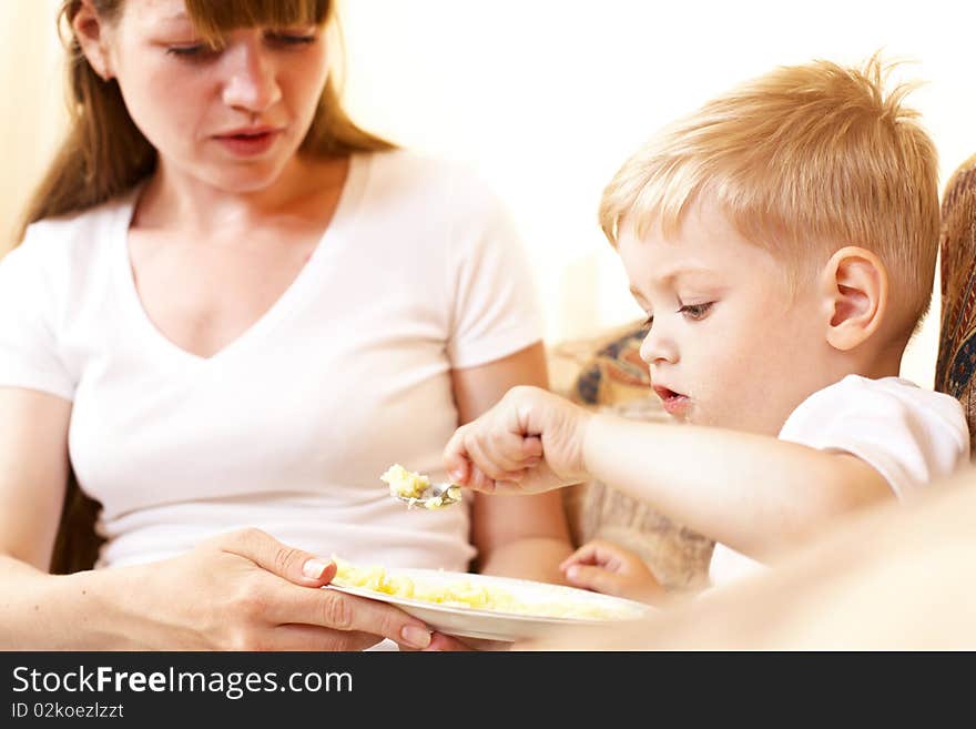 Mother feeding her little son at home; shallow DOF, focus on boys eyes. Mother feeding her little son at home; shallow DOF, focus on boys eyes