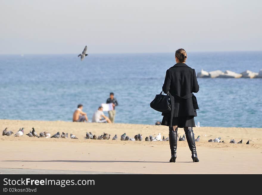 Woman looking for the sea at the Barceloneta sea beach in Barcelona, Spain; focus on the women' figure, background is blurred by lens defocusing. Woman looking for the sea at the Barceloneta sea beach in Barcelona, Spain; focus on the women' figure, background is blurred by lens defocusing