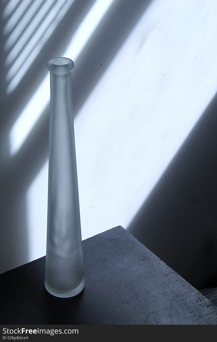 Thin bottle in front of a white wall with blind shadows