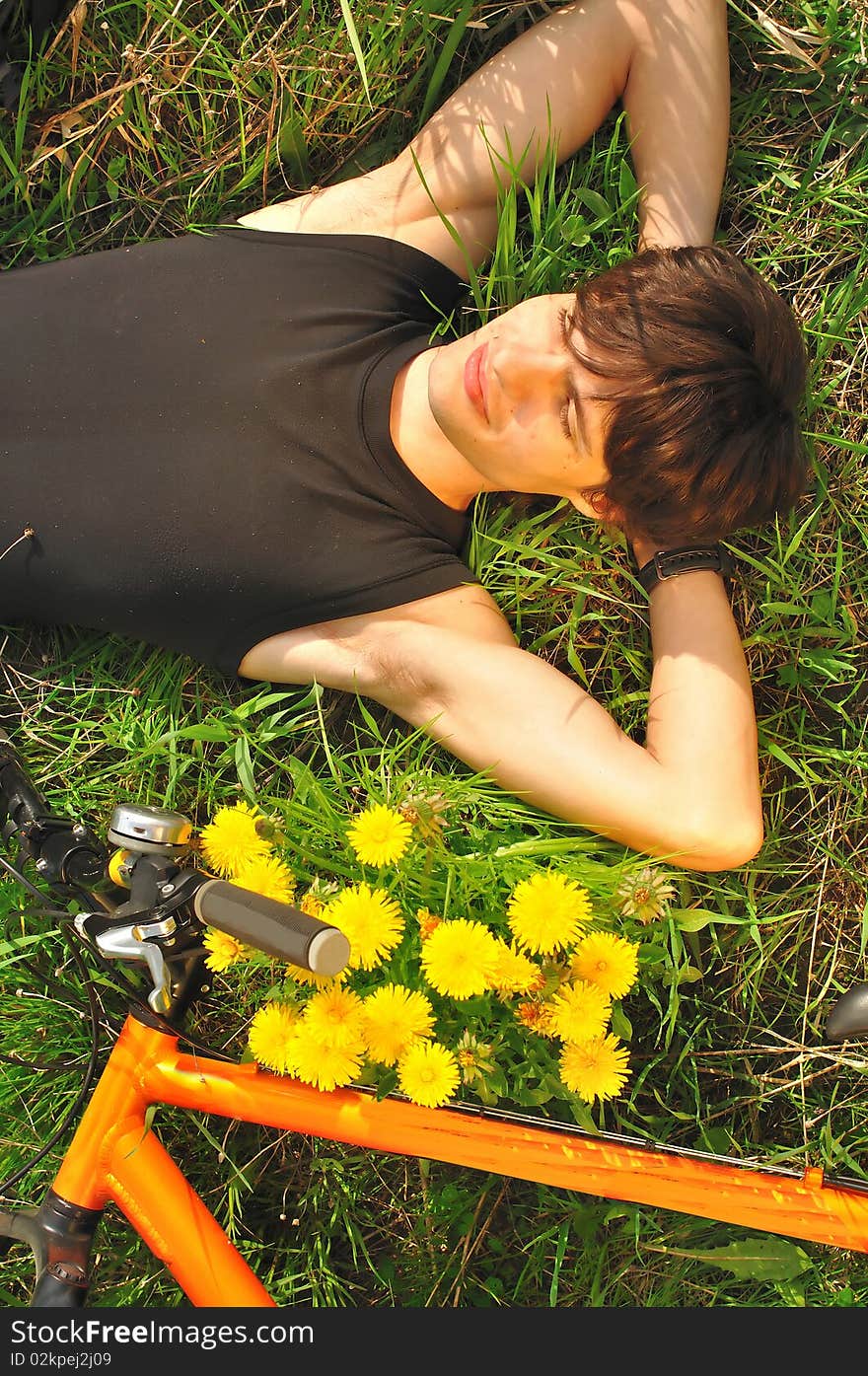 a smiling young man lying on the ground with eyes closed, in the bottom of the picture there is a bicycle; warm lighting setup. a smiling young man lying on the ground with eyes closed, in the bottom of the picture there is a bicycle; warm lighting setup