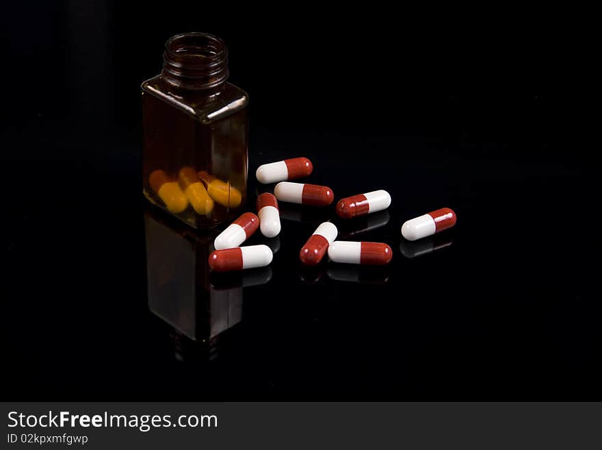 Medical pills and a prescription bottle on a reflective black background