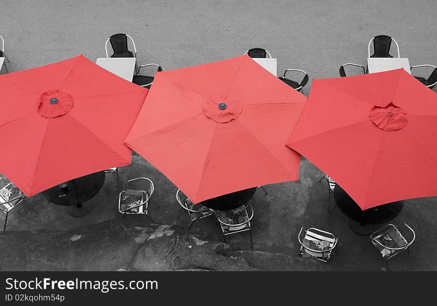 Large red umbrellas in street cafe viewed from above.