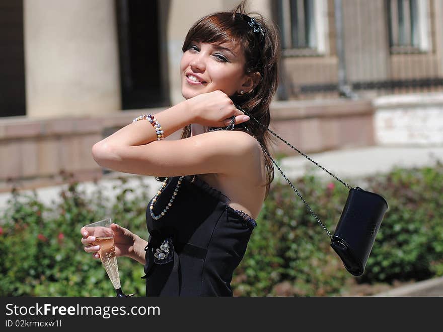 The young woman with a glass of a champagne in the street