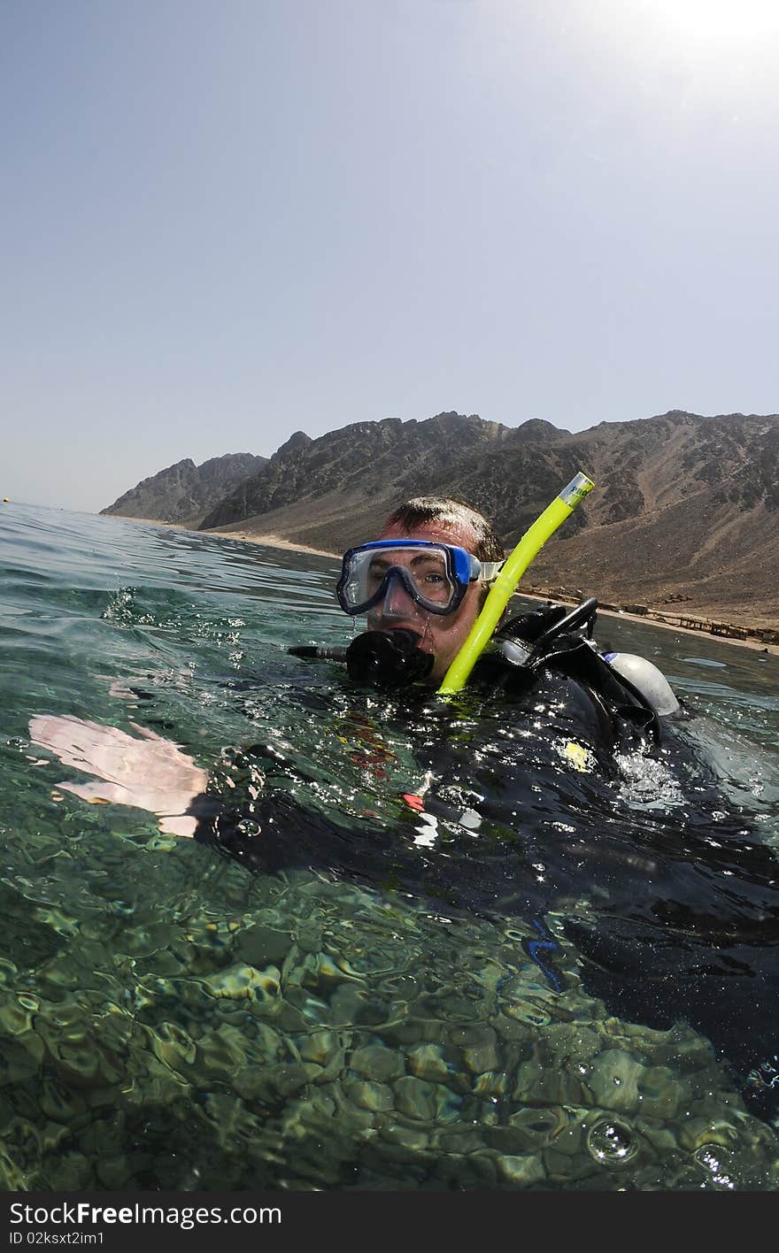 Male scuba diver on surface with mountains behind. Male scuba diver on surface with mountains behind