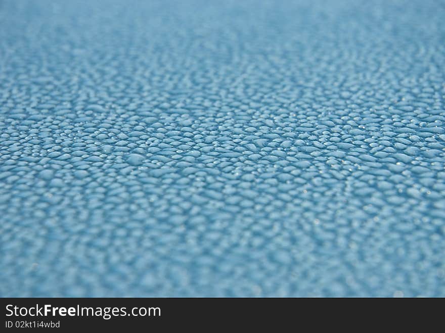 Close-up shot of dew drops on a light blue or turquoise metallic surface, glistening from the light. Close-up shot of dew drops on a light blue or turquoise metallic surface, glistening from the light