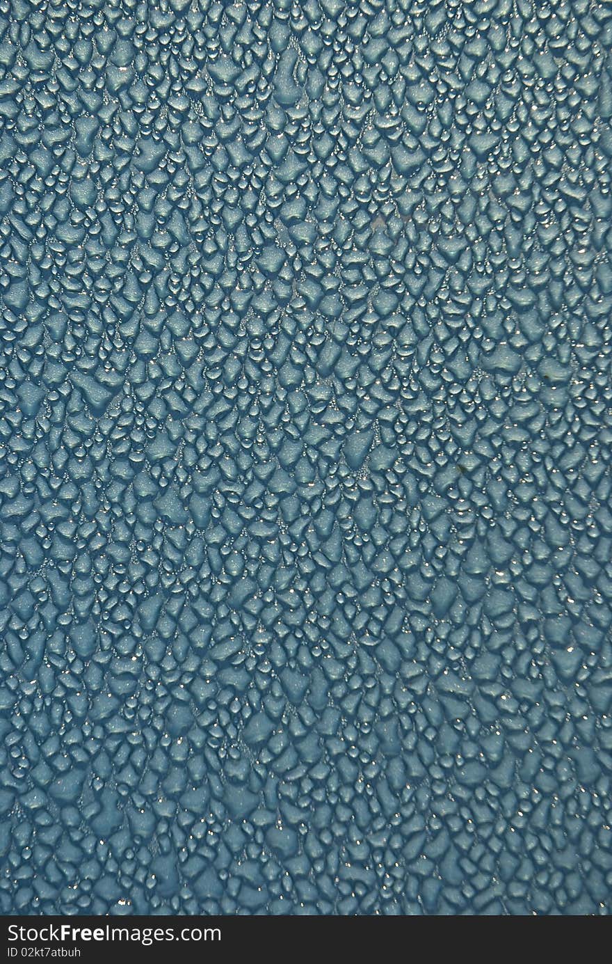 Close-up shot of dew drops on a light blue or turquoise metallic surface, glistening from the light. Close-up shot of dew drops on a light blue or turquoise metallic surface, glistening from the light