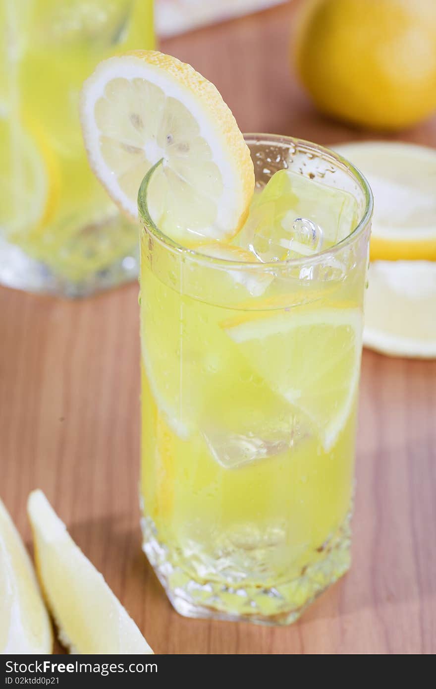 Glass of cold lemon beverage with slices of lemon fruit on wooden table top. Glass of cold lemon beverage with slices of lemon fruit on wooden table top