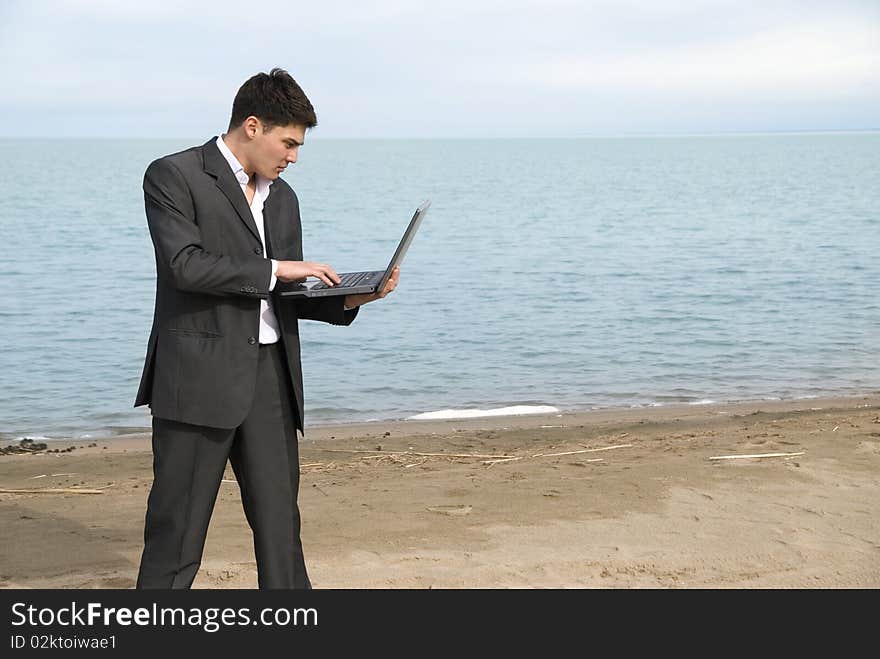 Young guy in a suit with a laptop on the beach. Young guy in a suit with a laptop on the beach