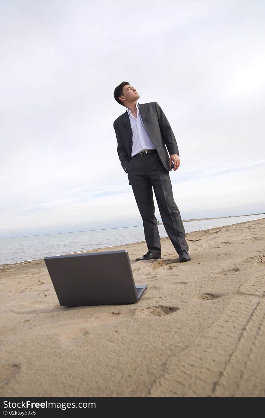 Guy in a suit standing on the beach looking up. before him laptop. Guy in a suit standing on the beach looking up. before him laptop