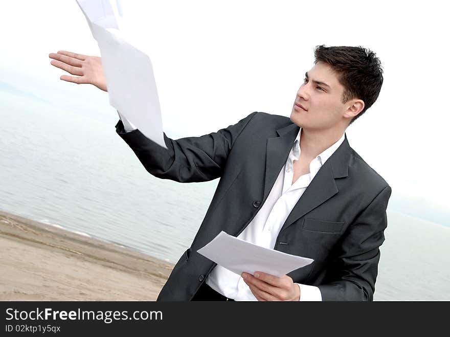 Young guy in a business suit with joy throwing papers on the beach. Young guy in a business suit with joy throwing papers on the beach