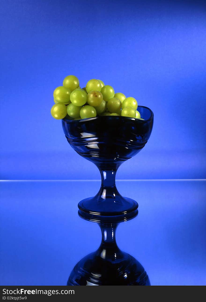 Green grapes in glass bowl isolated on mirrow and blue background