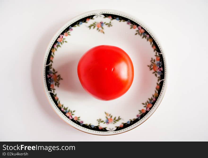 The tomato lies in a saucer on a white background