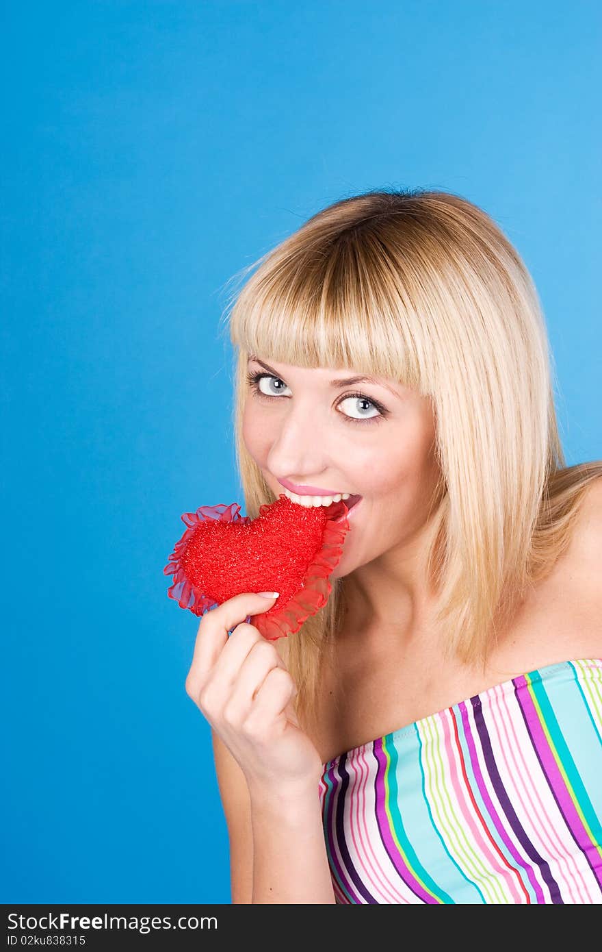 Attractive woman biting a red heart over blue background. Attractive woman biting a red heart over blue background