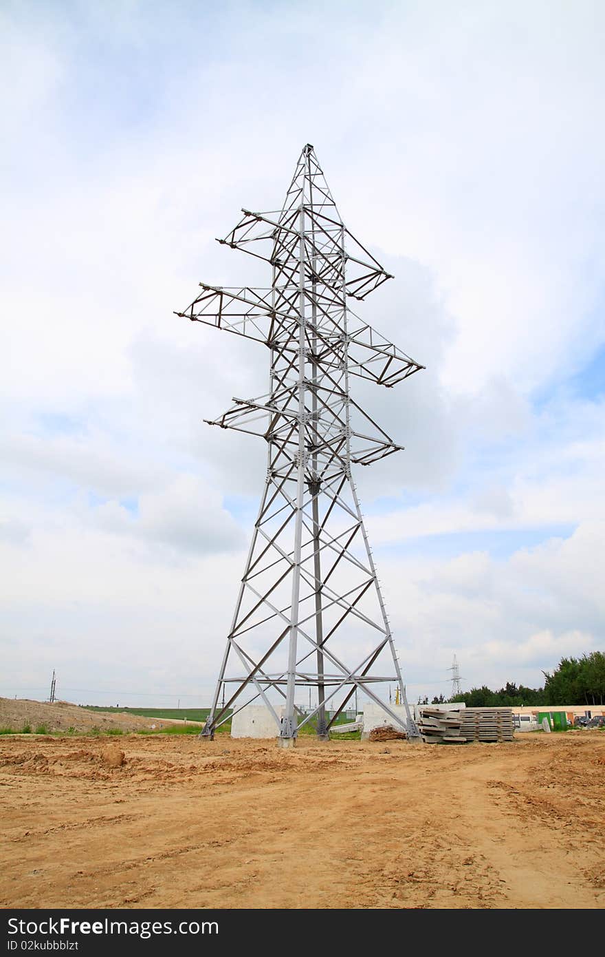 The high-voltage support standing on the earth, against the blue sky