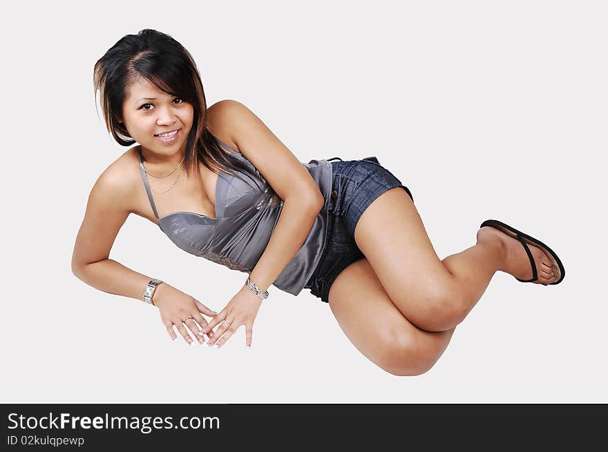 A young pretty Cambodian woman, in shorts and silver gray top, lying on the floor in the studio and looking into the camera, on white background. A young pretty Cambodian woman, in shorts and silver gray top, lying on the floor in the studio and looking into the camera, on white background.